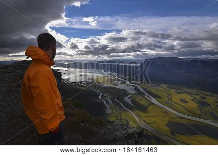 Male hiker enjoying the view over rapadalen river delta in rainy landscape