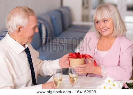 I wonder what is in there. Attractive emotional elderly woman being delighted by her gentelmans gift while holding it and sitting at the table in a restaurant