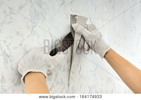 removing old wallpapers from wall with spatula during repair