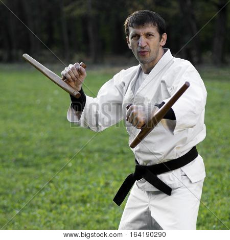 Master of martial arts in white kimono is practicing with tonfa.