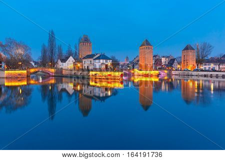 Medieval towers and bridges Ponts Couverts with mirror reflections in Petite France during twilight blue hour, Strasbourg, Alsace, France