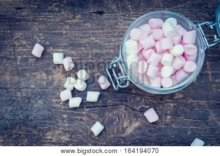 Pink and white mini marshmallows in a jar on an old rustic wooden table with space for text. Mini white and pink puffy marshmallows. Marshmallow concept. Copy space. Top view.