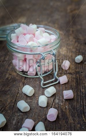 Pink and white mini marshmallows in a jar on an old rustic wooden table with space for text. Mini white and pink puffy marshmallows. Marshmallow concept. Copy space. Selective focus.
