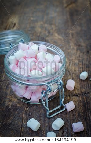 Pink and white mini marshmallows in a jar on an old rustic wooden table with space for text. Mini white and pink puffy marshmallows. Marshmallow concept. Copy space. Selective focus.