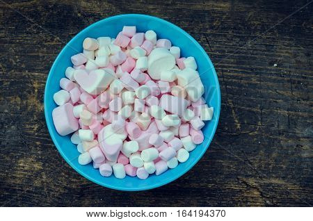 Colorful marshmallows in a bowl on an old rustic wooden table macro texture background with space for text. A pile of mini white pink and orange puffy marshmallows. Marshmallow concept. Copy space.