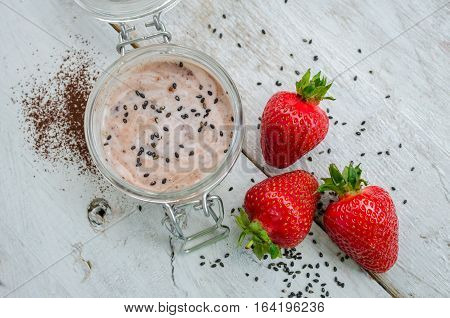 Homemade yogurt in a jar with strawberry seeds and cacao. Dessert with strawberries on a white wooden background. Fresh juicy strawberry with yogurt. Directly above. Top view. Horizontal.