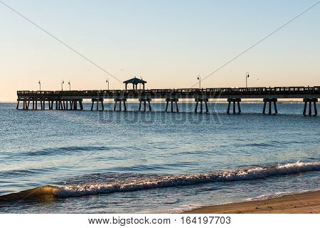 Fishing pier with waves at Buckroe Beach in Hampton, Virginia at sunrise.