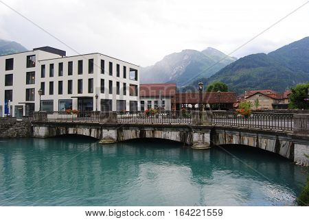 Interlaken, Switzerland - July 13, 2014. Bridge across the Aare river, connecting Interlaken to Unterseen, with historic and modern buildings and commercial properties, on a rainy evening.