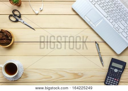 Top view laptop pen black coffee calculator stationary earphones cookies on office desk background.