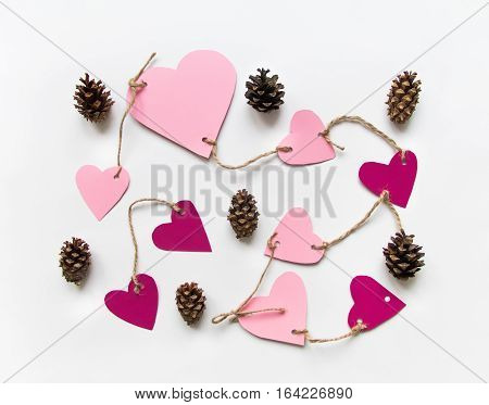 Bright pink paper hearts connected with a rope. Cards for Valentine's day decorated with cones. Flat lay on white background with place for text top view