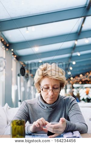 Mid age woman with mobile phone sitting at indoor cafe looking for screen