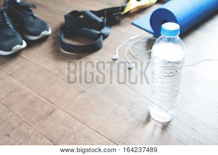 Fitness concept with bottle of water sneakers TRX yoga mat and earphones on wood floor Copy space