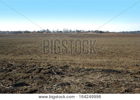 Country landscape with plowed field and a village far away on spring day