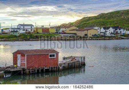 Little red shack on a dock in the small village and community of Twillingate, Newfoundland.  Sun sets brightly behind a hill in this coastal small Newfoundland community.