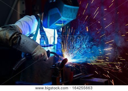 man in protective clothing welding metal in the factory