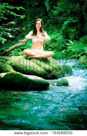a young beautiful lady is meditating by a river flowing through the forest