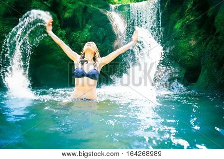 a young beautiful lady is enjoying the waterfall's cold water