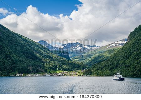 Ferry boat on it's way to small norwegian town. Fjord shores and snowy mountain peaks on the background. Norway cruise landscapes.