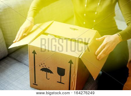 Elegant woman unpacking unboxing cardboard carton box with protective foam pads inside after buying ordering online via internet a present good with green illumination light coming from the box