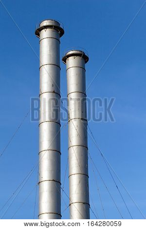Two high industrial smoke pipes over clear blue sky vertical view close up