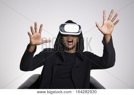 Portrait of an African American man wearing a black hoodie and virtual reality glasses. His mouth is open. His hands are in the air. Mockup