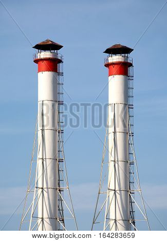 Two high industrial smoke pipes over clear blue sky vertical view close up