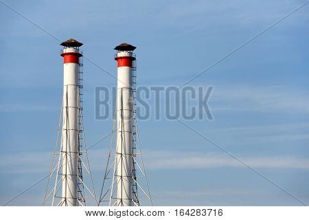 Two high white industrial smoke pipes over clear blue sky horizontal view close up
