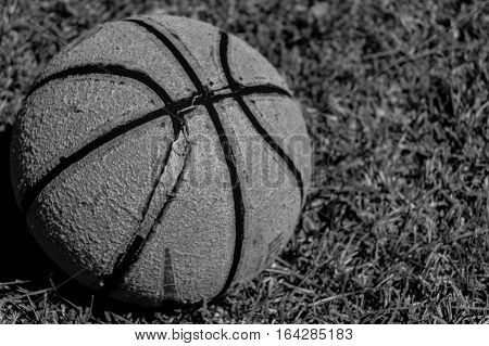 Worn out basketball sitting in the grass in black and white.