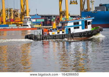 tugboat assisting bulk cargo ship to harbor freight and yellow crane