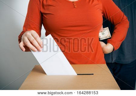 adult woman casting her vote while getting some cash us dollars from a guy standing behind her.