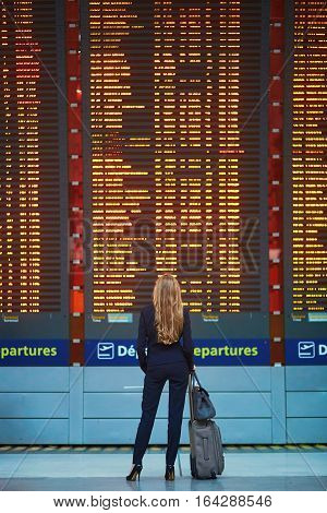 Woman With Hand Luggage In International Airport Terminal, Looking At Information Board