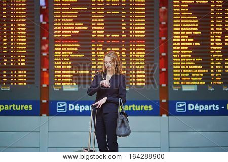 Woman With Hand Luggage In International Airport Terminal, Looking At Information Board