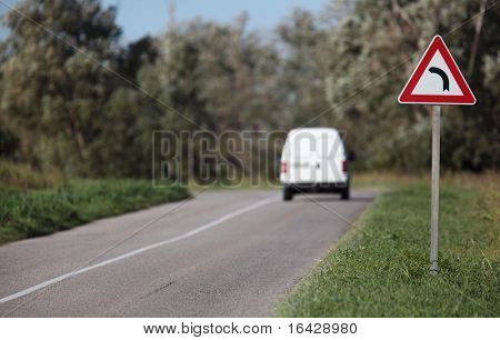 White pick-up going on a contryside road with a sharp corner sign on a lovely day