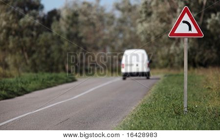 White pick-up going on a contryside road with a sharp corner sign on a lovely day