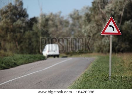 White pick-up going on a contryside road with a sharp corner sign on a lovely day