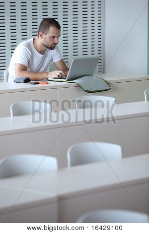 Junge männliche College-Studenten, die Arbeiten auf seinem Laptopcomputer in einem Klassenzimmer