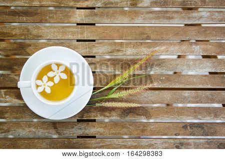 Cup of tea & couple of white flowers & group of Cenchrus setaceus grass flowers on wooden table with blurry bokeh in the background. Have a lot of text space for your project.