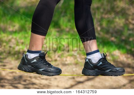 Tightrope walker is on a tight sling which is fixed on the trees at a low altitude. Slasklining extreme sport a balancing act.