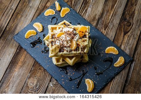 Photo of several Belgian waffles with chocolate, tangerines and ice-cream on blackboard