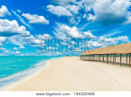 Beautiful tropical sandy beach with canopies from the sun and blue cloudy sky