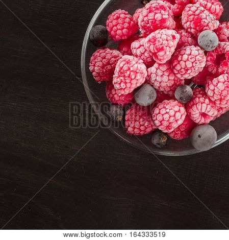Frozen raspberries in a glass saucer. Frost on the berries. Dark background.