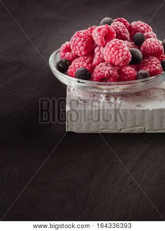 Frozen raspberries in a glass saucer. Frost on the berries. Dark background.