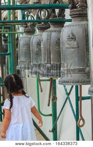 Girl white shirt with row of bells in buddhist temple in Thailand. Buddhist temple bells. Bells of the old temple in Thailand