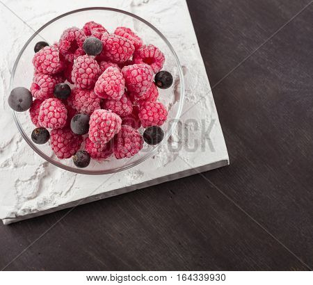 Frozen raspberries in a glass saucer. Frost on the berries. Dark background.