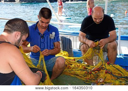 BALI, CRETE - SEPTEMBER 16, 2016 - Three Cretan fishermen tending to their fishing nets on a small fishing boat in the harbour Bali Crete Greece Europe, September 16, 2016.