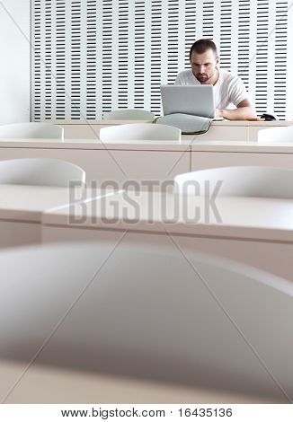 Junge männliche College-Studenten, die Arbeiten auf seinem Laptopcomputer in einem Klassenzimmer