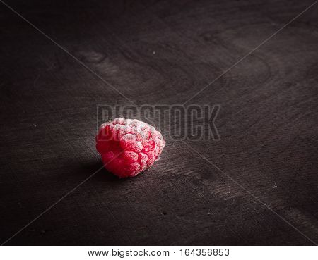 Frozen raspberrieson dark wood. Frost on the berries. Red and black.