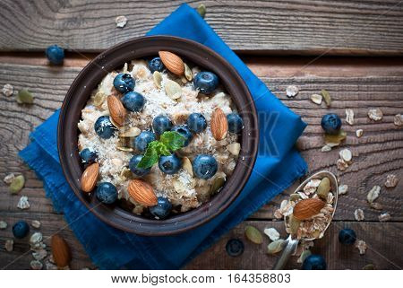 Oatmeal with blueberries, almonds, coconat and seeds at rustic wooden table. Flat lay.