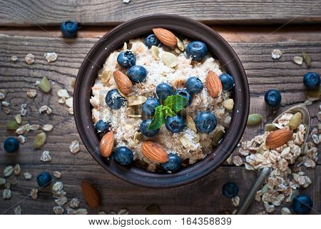 Oatmeal with blueberries, almonds, coconat and seeds at rustic wooden table. Flat lay.