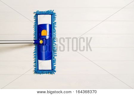 Cleaning floor with mop top view. Microfiber mop isolated on white wooden floor background. Home cleaning product concept photograph with copy space